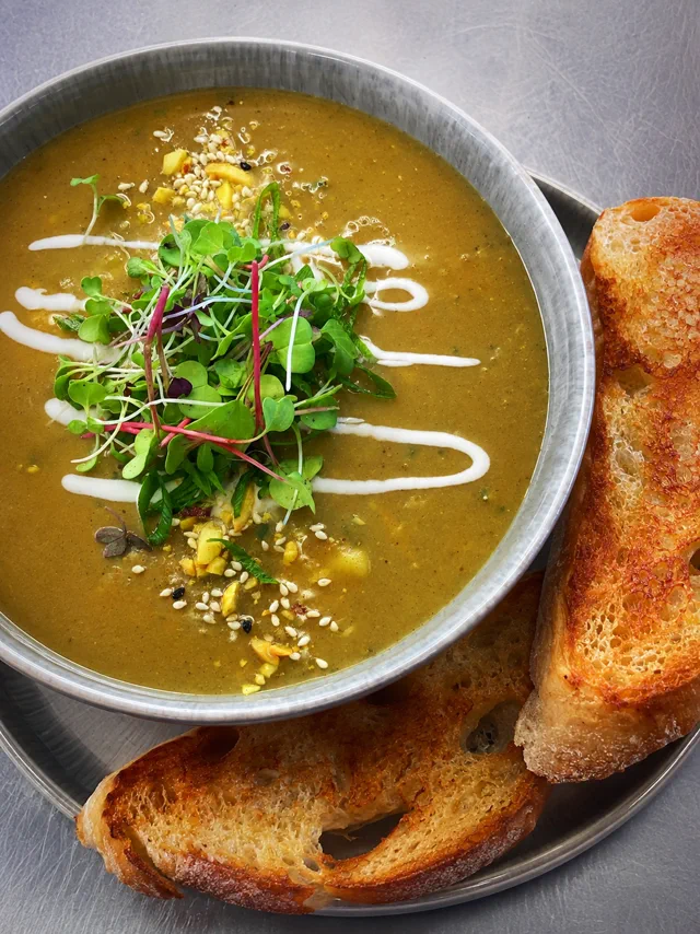 A warm bowl topped with greens and served with toasted bread